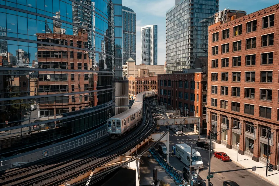 High view of Chicago train on elevated rail in downtown with reflective glass building on left and brick building on right.